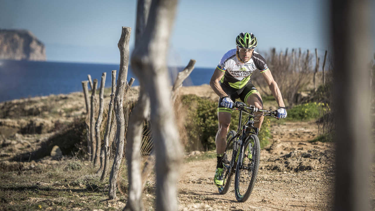 Mann im Grünen Und Schwarzen Fahrradhelm, Der Tagsüber Auf Dem Fahrrad in Der Nähe Des Braunen Baumstamms Fährt. Wallpaper in 1280x720 Resolution