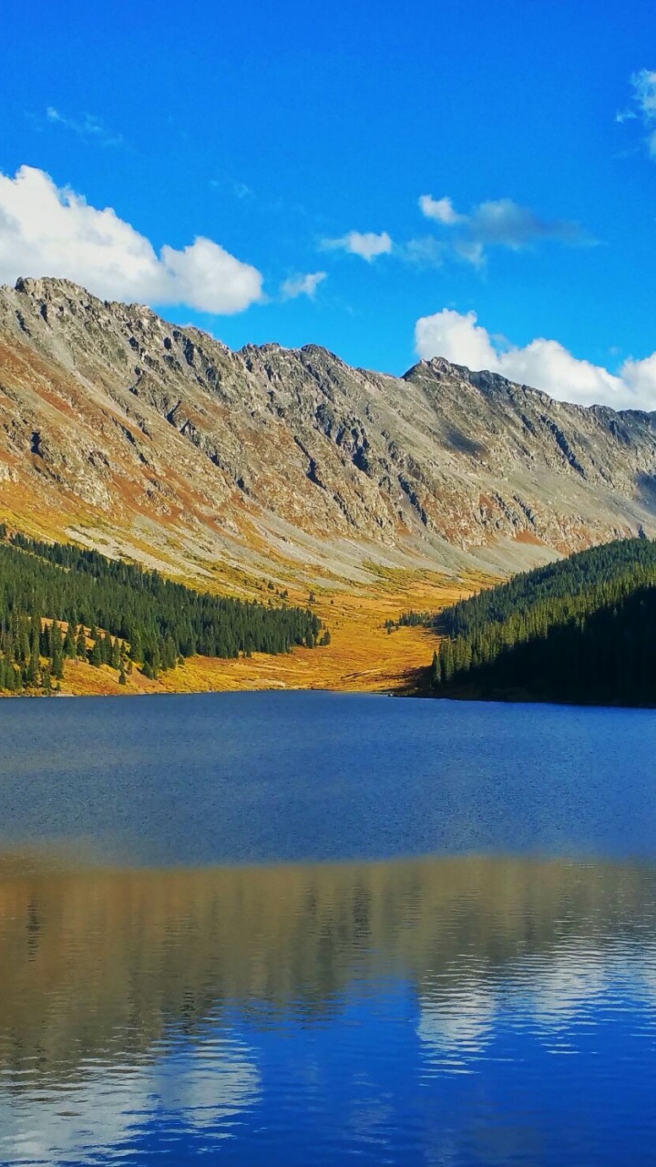 Tagsüber Grüne Und Braune Berge Neben Dem See Unter Blauem Himmel. Wallpaper in 720x1280 Resolution
