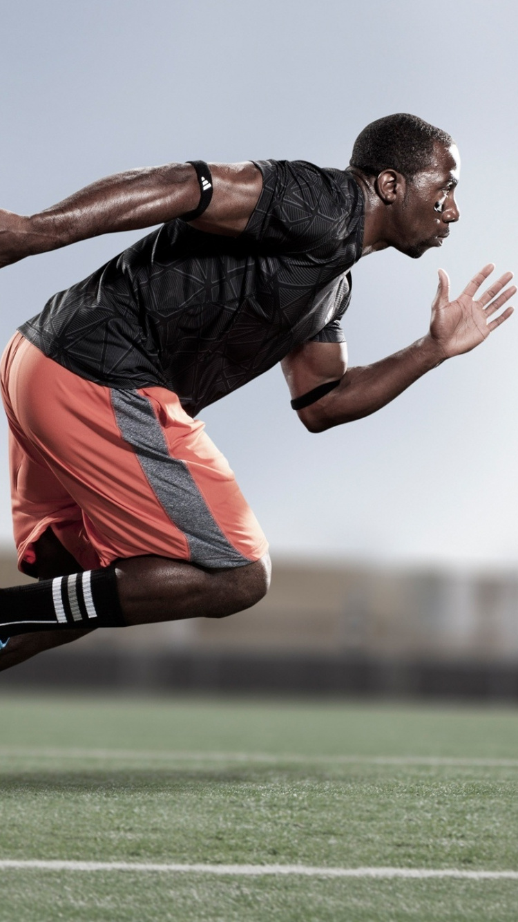 Homme en T-shirt Noir et Short Orange Sautant Sur le Terrain D'herbe Verte Pendant la Journée. Wallpaper in 750x1334 Resolution
