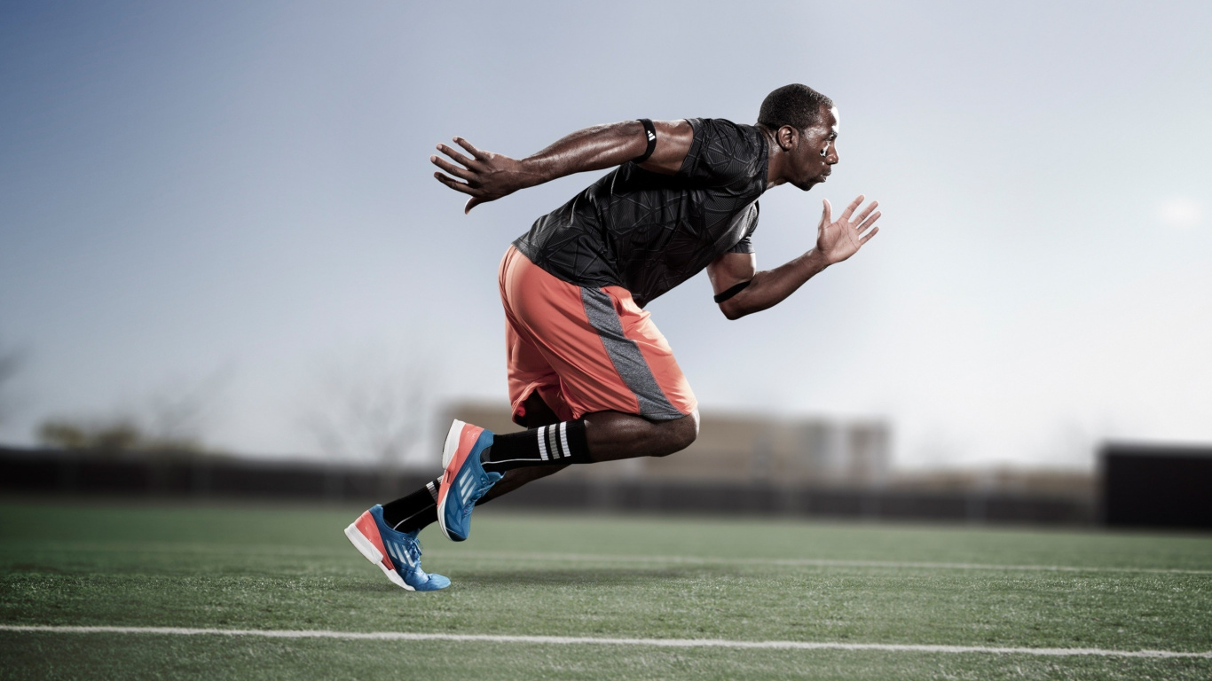 Man in Black T-shirt and Orange Shorts Jumping on Green Grass Field During Daytime. Wallpaper in 1366x768 Resolution