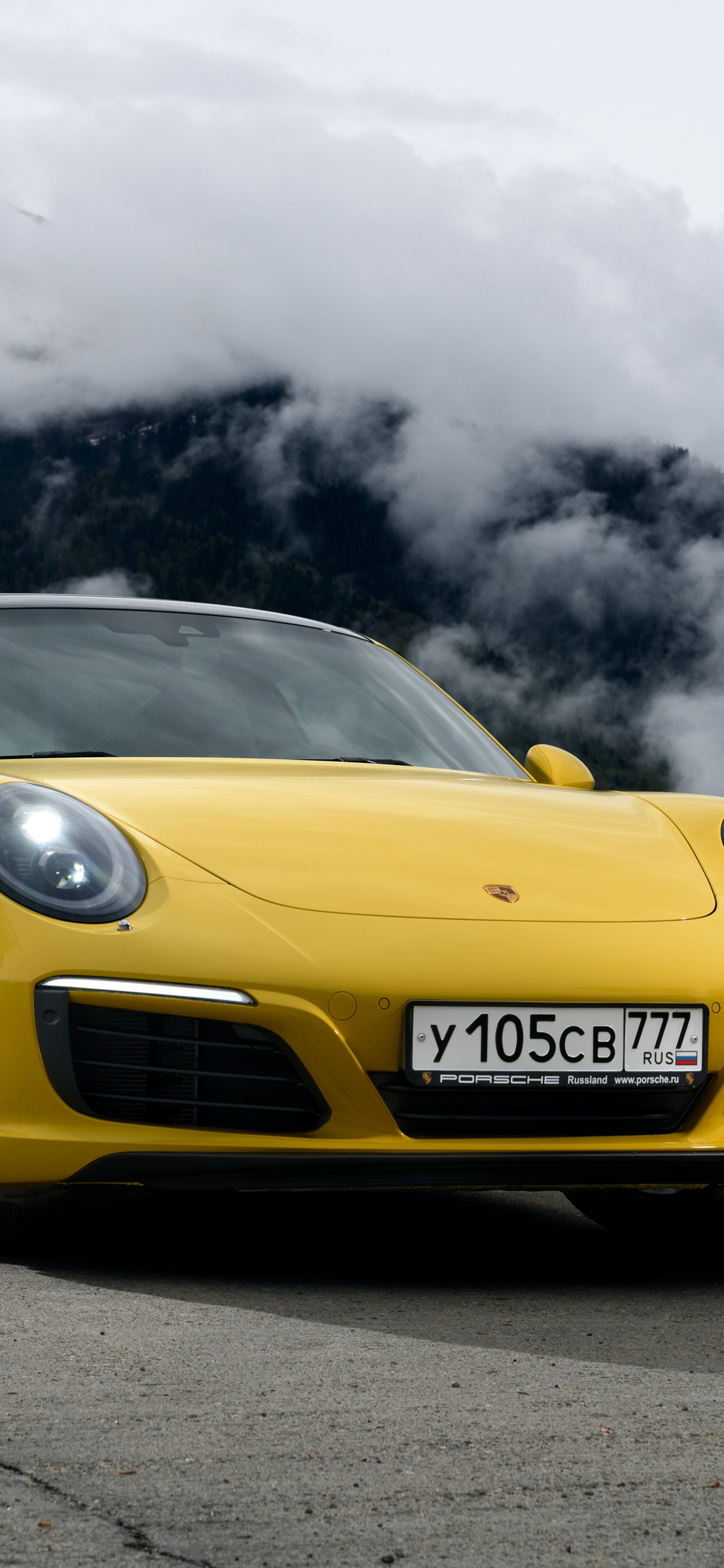 Yellow Porsche 911 on Black Asphalt Road Under Gray Clouds. Wallpaper in 1242x2688 Resolution