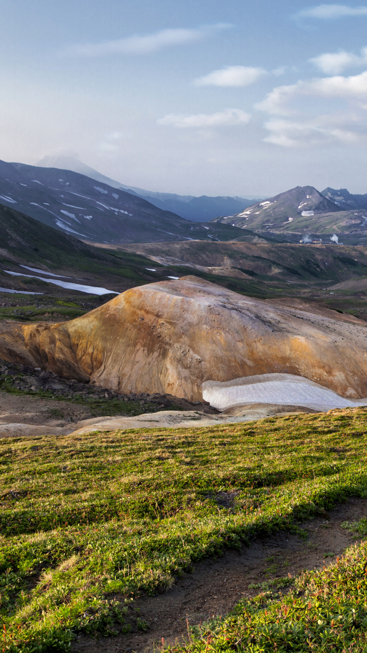 Grünes Grasfeld in Der Nähe Des Braunen Berges Unter Weißen Wolken Tagsüber. Wallpaper in 750x1334 Resolution