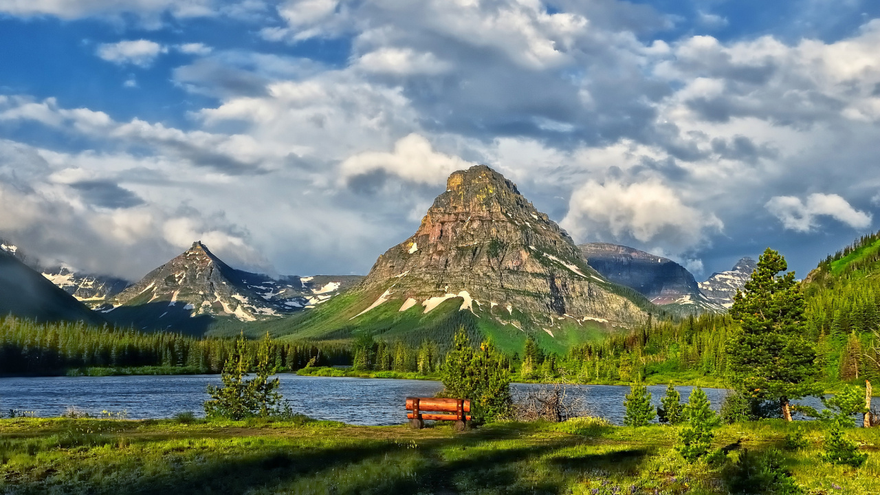 Brown Wooden Bench on Green Grass Field Near Lake and Mountain Under White Clouds and Blue. Wallpaper in 1280x720 Resolution
