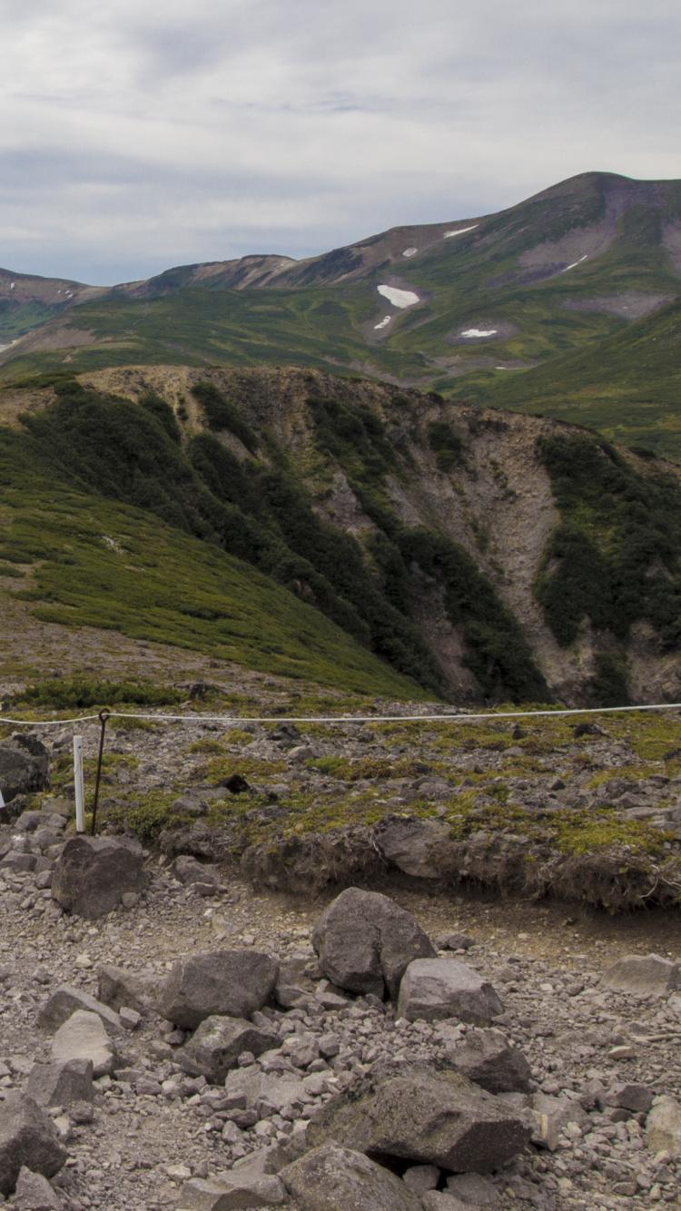 Champ D'herbe Verte Près de la Montagne Sous Des Nuages Blancs Pendant la Journée. Wallpaper in 750x1334 Resolution