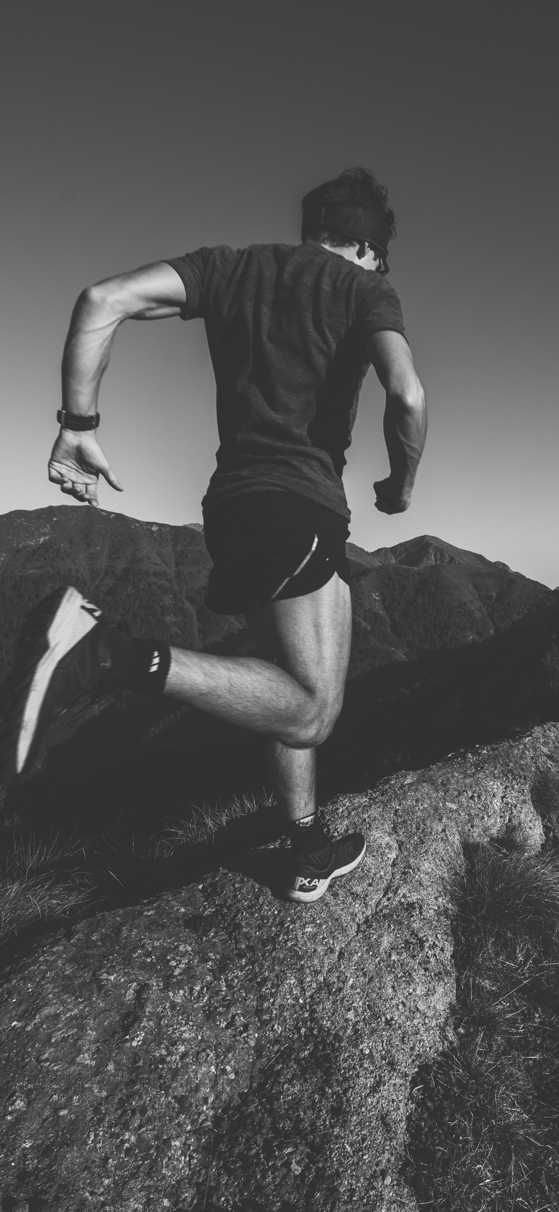 Man in Black T-shirt and Black Shorts Sitting on Rock. Wallpaper in 1125x2436 Resolution