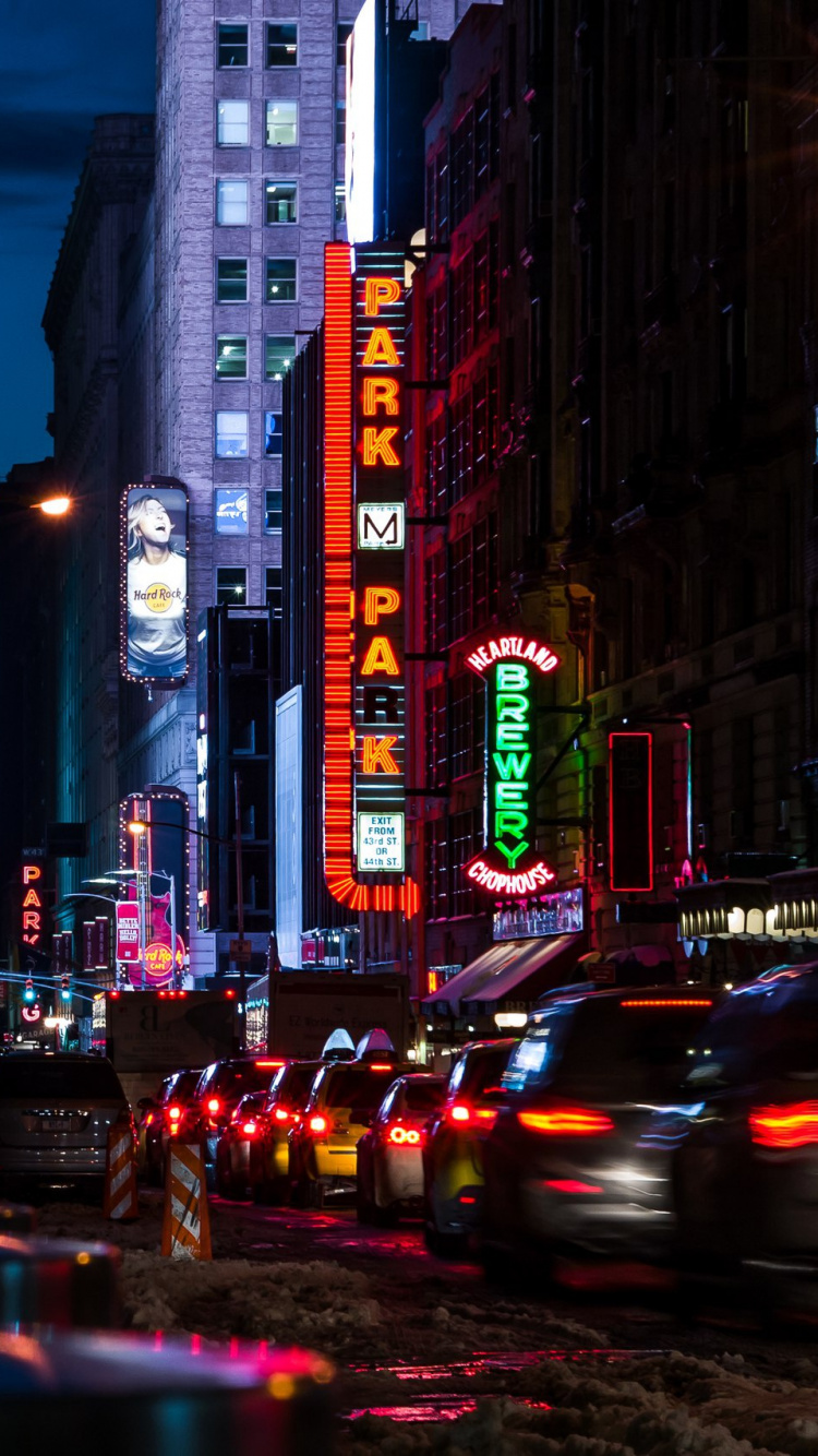 Autos Auf Der Straße Zwischen Hochhäusern Während Der Nacht. Wallpaper in 750x1334 Resolution