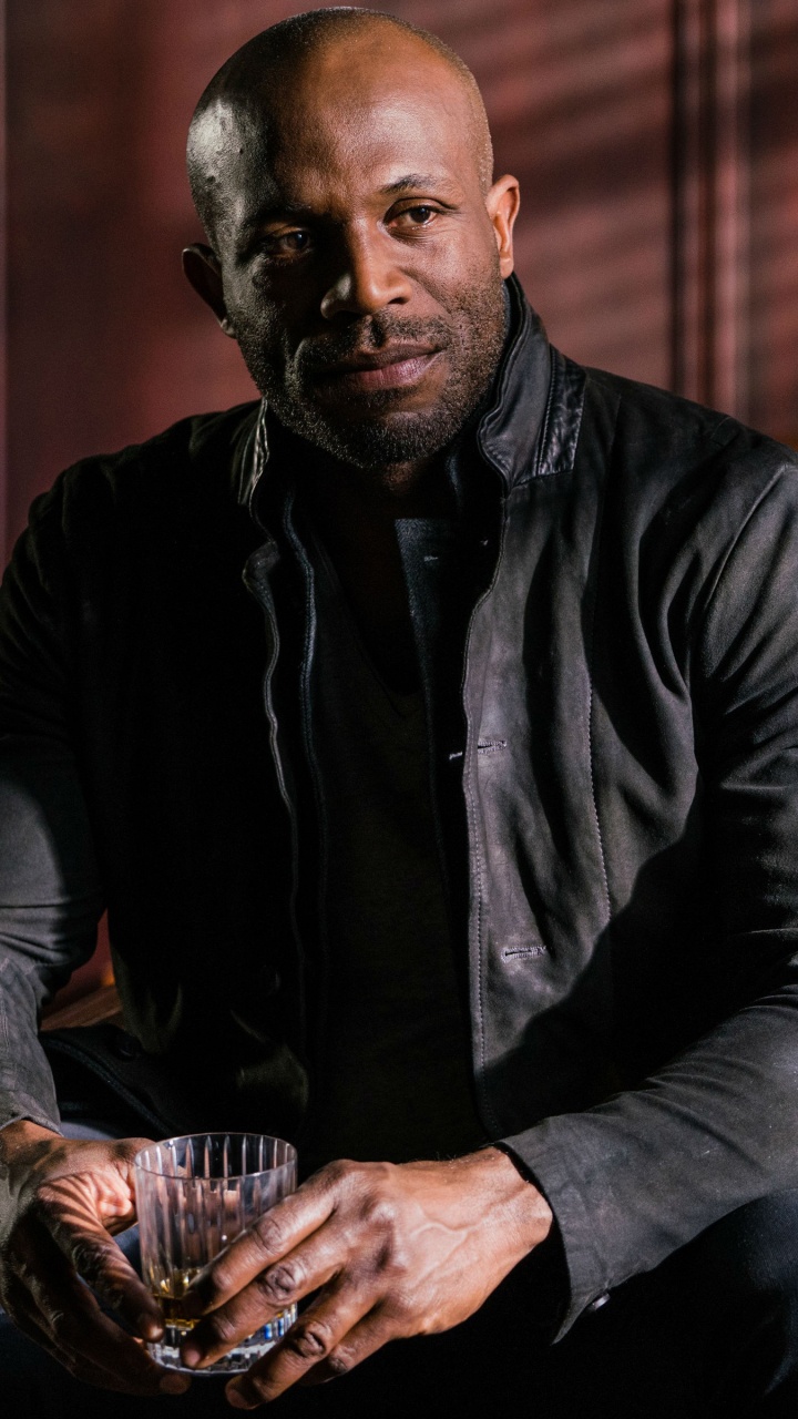 Man in Black Dress Shirt and Blue Denim Jeans Sitting on Brown Wooden Armchair. Wallpaper in 720x1280 Resolution