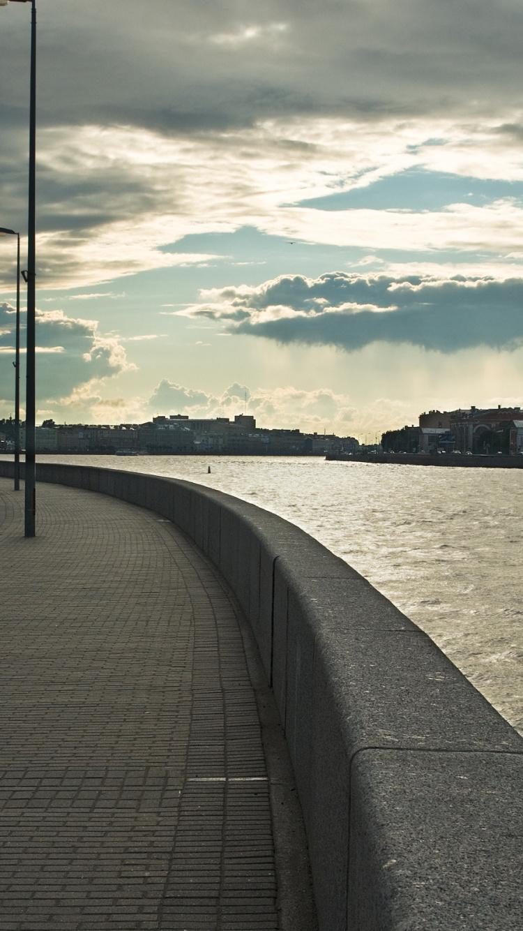 Camino de Hormigón Gris Cerca Del Cuerpo de Agua Bajo un Cielo Nublado Durante el Día. Wallpaper in 750x1334 Resolution