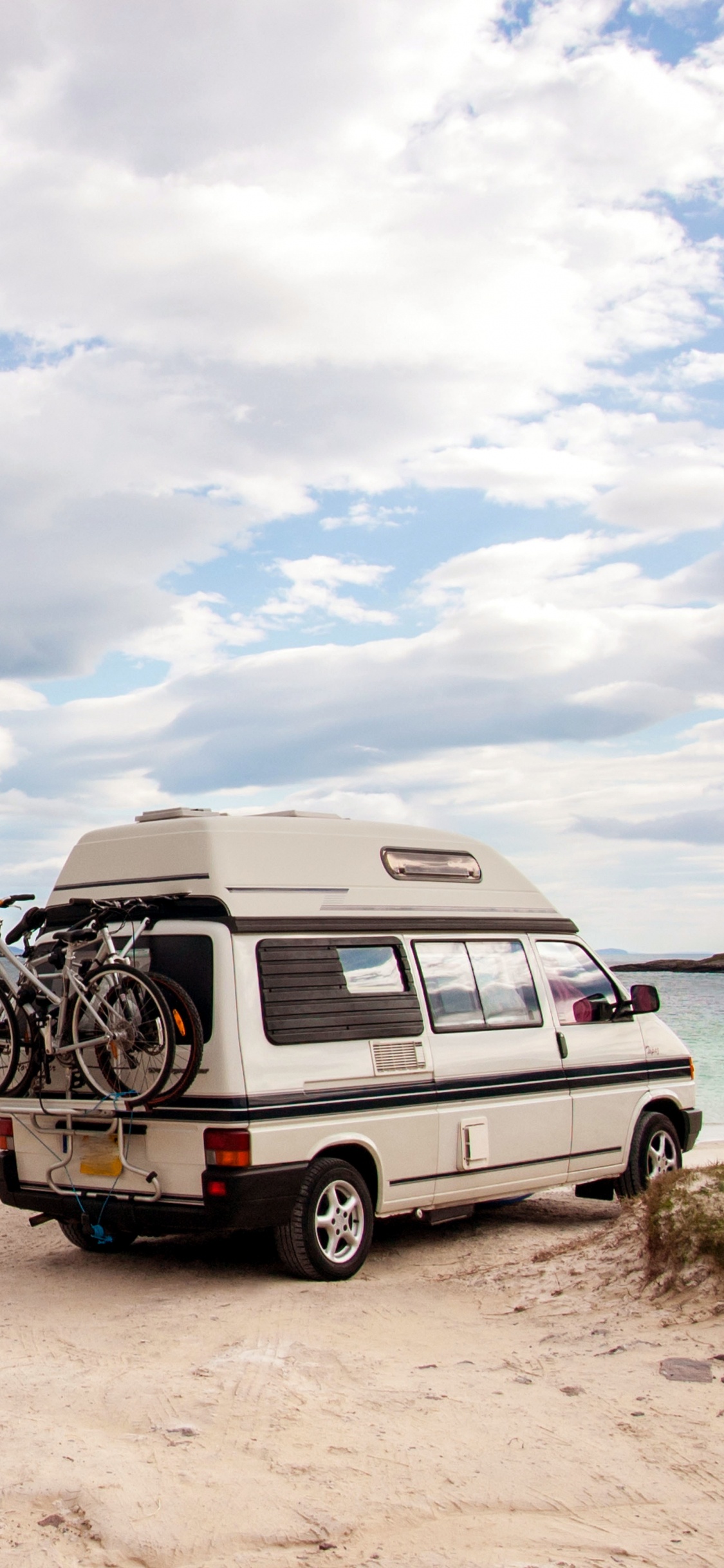 White and Black Van on Brown Sand Near Body of Water During Daytime. Wallpaper in 1125x2436 Resolution