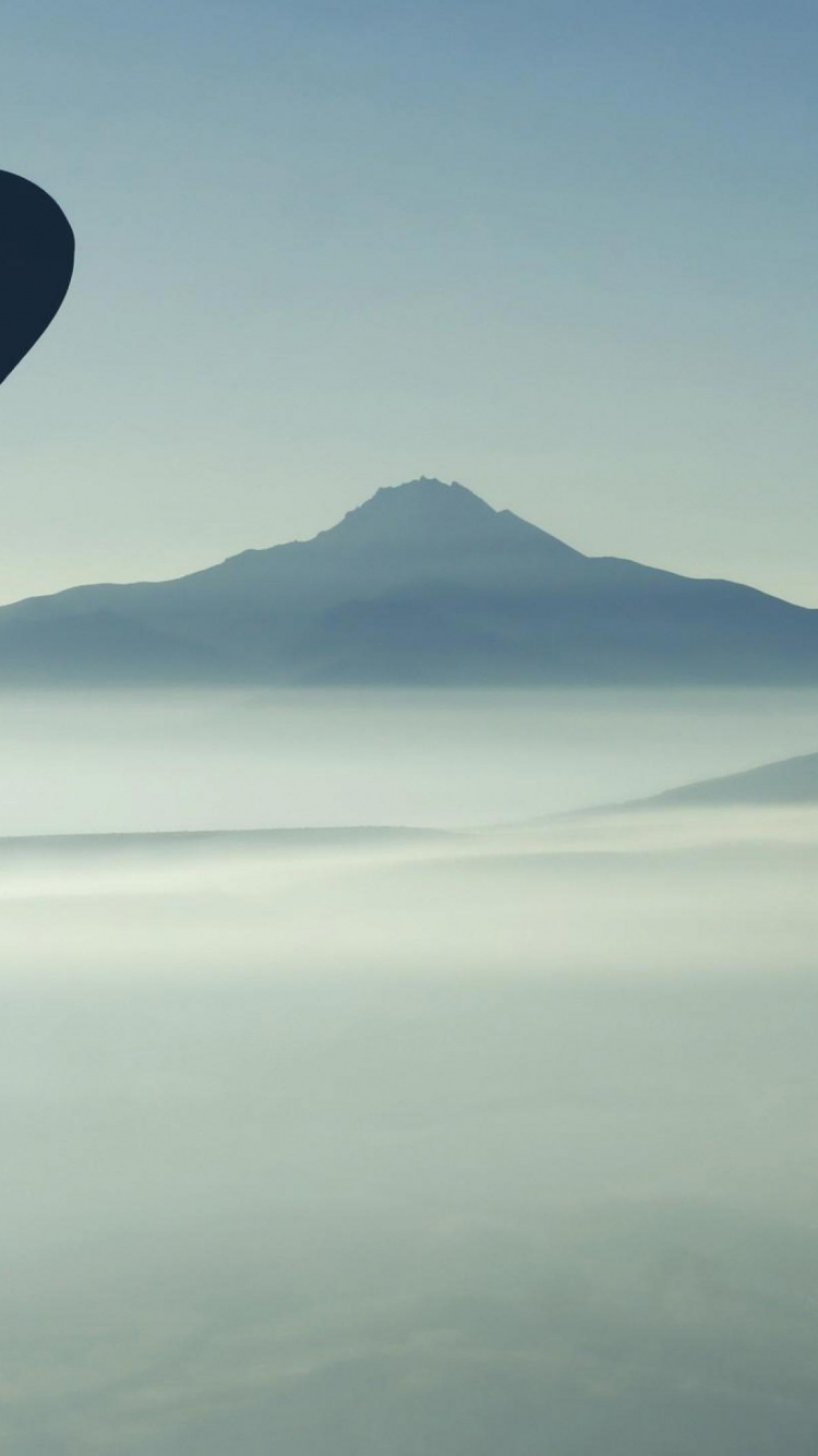 Blue Hot Air Balloon Flying Over The Mountains During Daytime. Wallpaper in 750x1334 Resolution