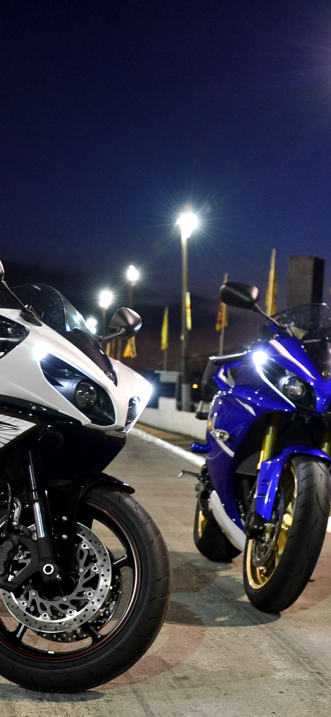 Black and White Sports Bike Parked Beside Yellow and White Bus During Night Time. Wallpaper in 1125x2436 Resolution