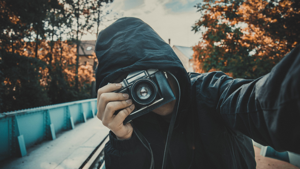 Man in Black Hoodie Holding Black Camera. Wallpaper in 1280x720 Resolution