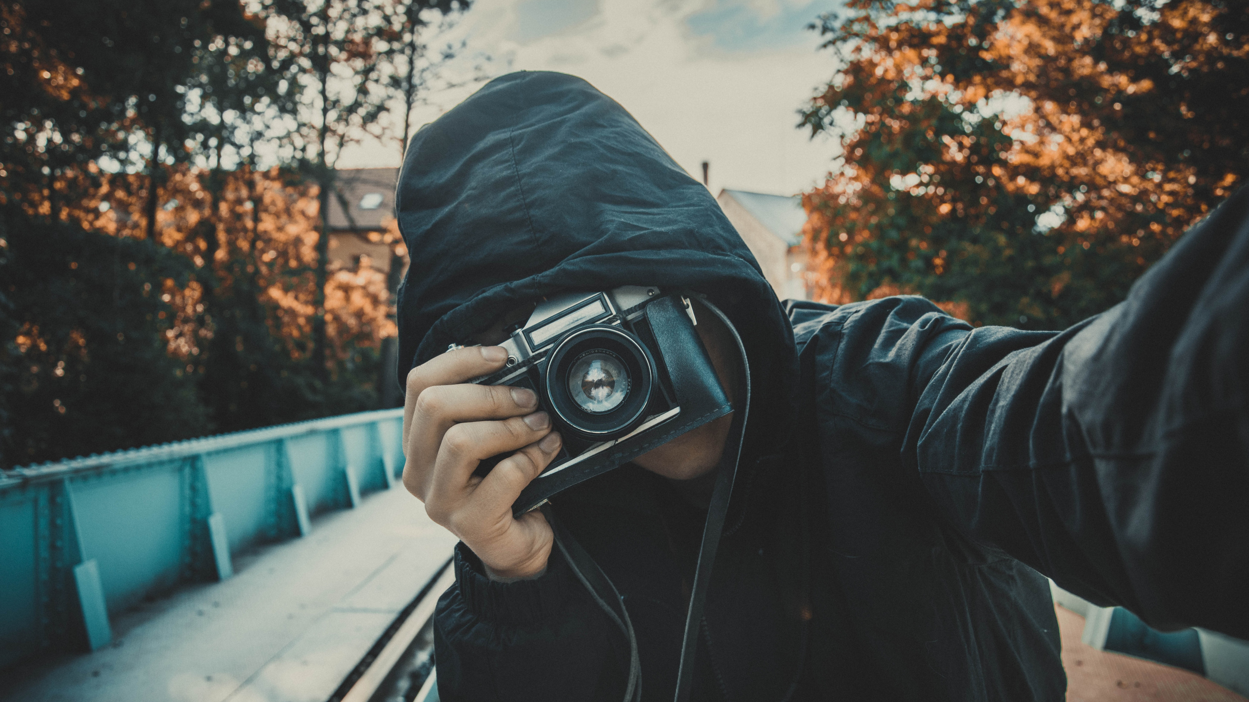 Man in Black Hoodie Holding Black Camera. Wallpaper in 2560x1440 Resolution