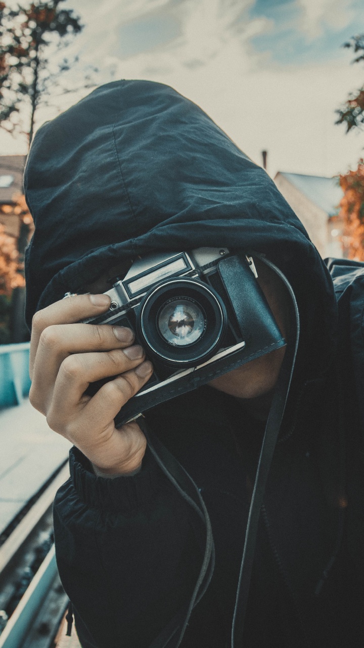 Man in Black Hoodie Holding Black Camera. Wallpaper in 720x1280 Resolution