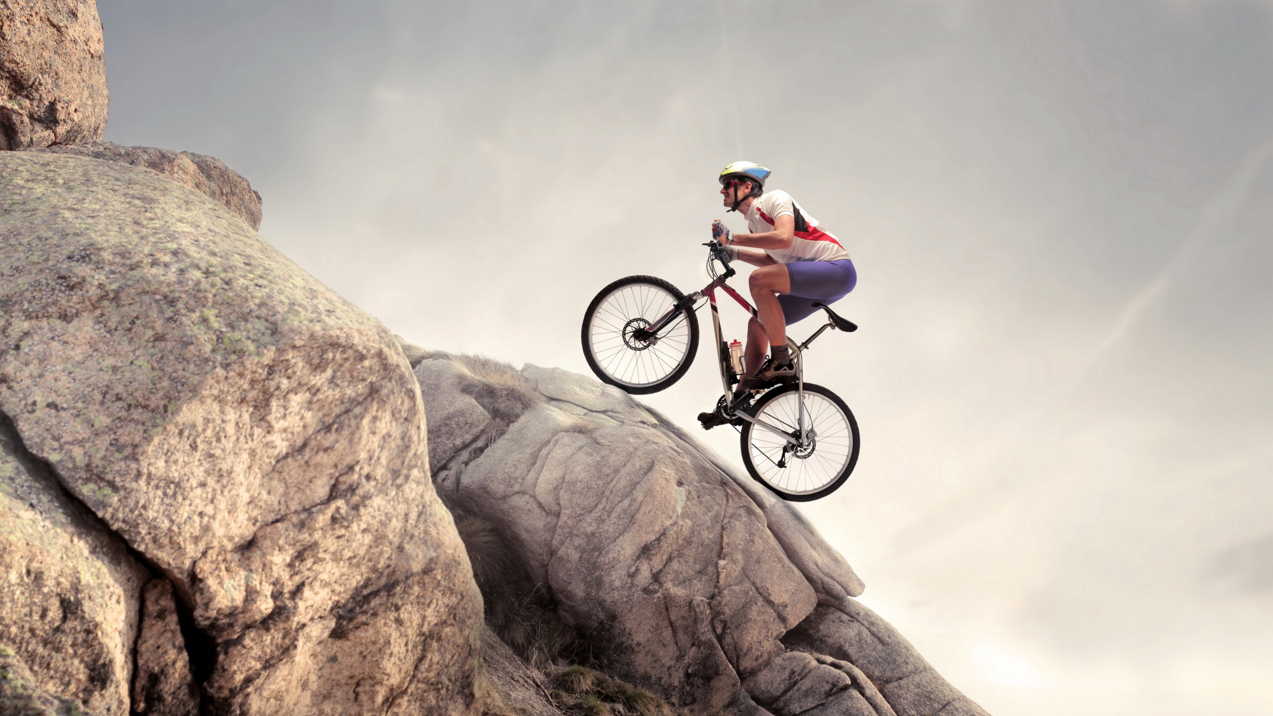 Man in Green Shirt Riding on Black Mountain Bike on Brown Rocky Mountain During Daytime. Wallpaper in 2560x1440 Resolution