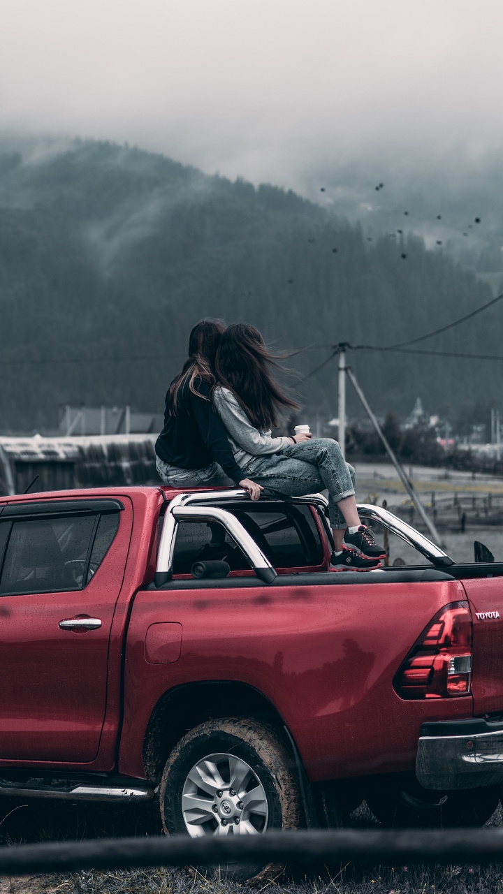 Woman in Black Jacket Sitting on Red Car Hood During Daytime. Wallpaper in 720x1280 Resolution