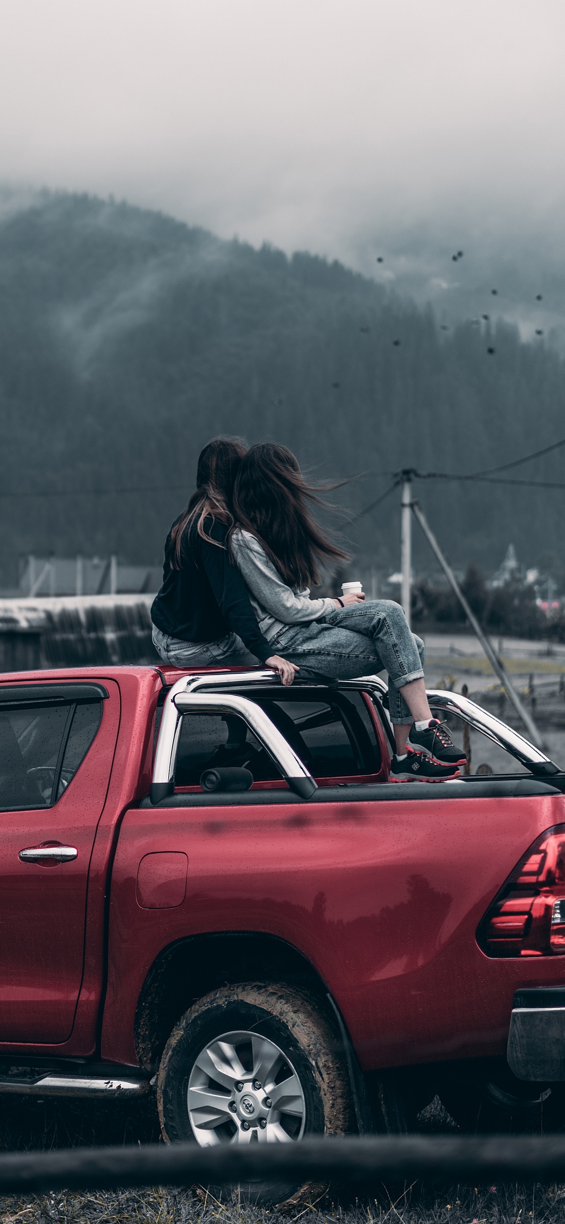 Femme en Veste Noire Assise Sur un Capot de Voiture Rouge Pendant la Journée. Wallpaper in 1125x2436 Resolution