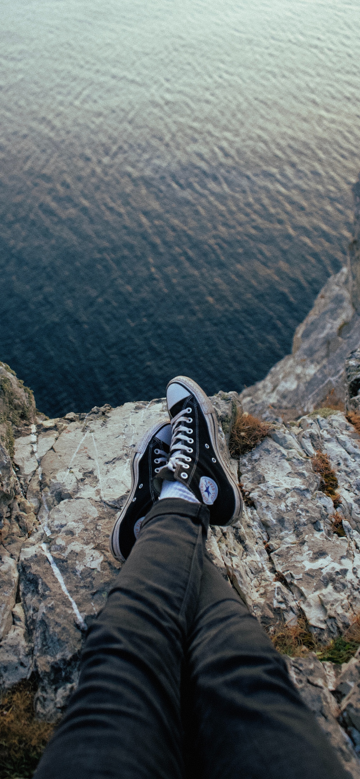 Personne en Pantalon Noir et Baskets Nike Noir et Blanc Assis Sur un Rocher. Wallpaper in 1242x2688 Resolution