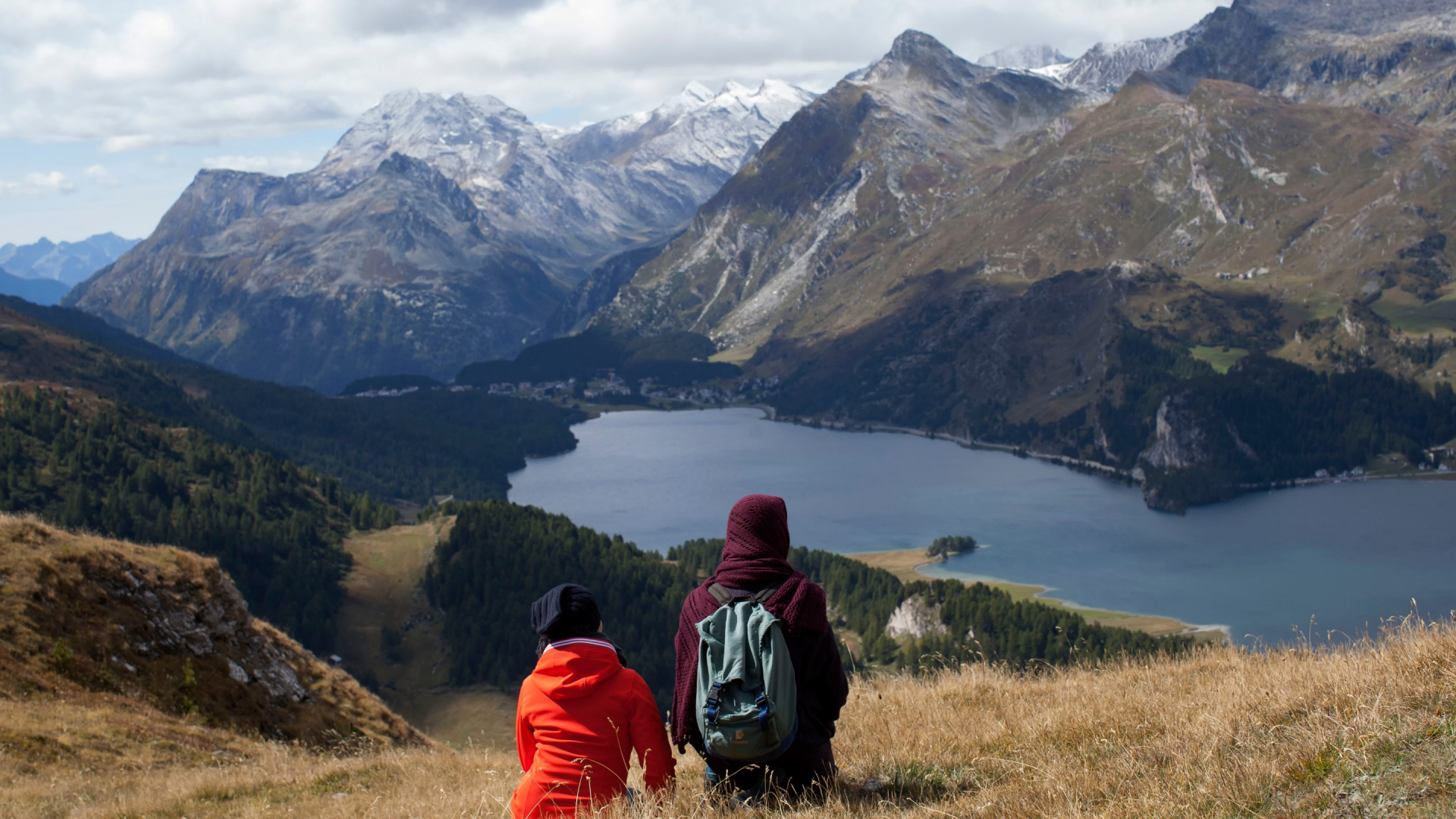 Personne en Sweat à Capuche Rouge et Noir Assis Sur un Terrain D'herbe Verte Près du Lac et Des Montagnes Pendant. Wallpaper in 1920x1080 Resolution