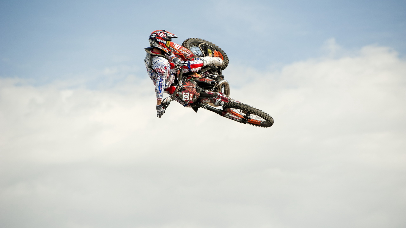 Hombre Montando Motocross Dirt Bike Haciendo Acrobacias Bajo Las Nubes Blancas Durante el Día. Wallpaper in 1366x768 Resolution