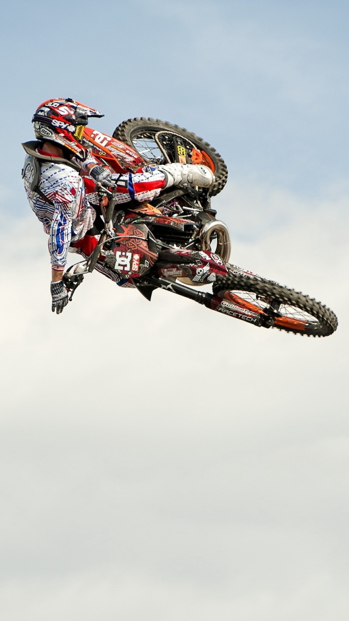 Hombre Montando Motocross Dirt Bike Haciendo Acrobacias Bajo Las Nubes Blancas Durante el Día. Wallpaper in 720x1280 Resolution