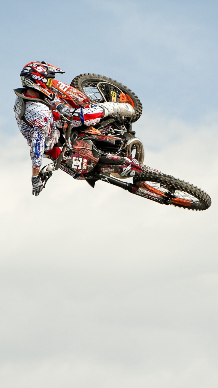 Hombre Montando Motocross Dirt Bike Haciendo Acrobacias Bajo Las Nubes Blancas Durante el Día. Wallpaper in 750x1334 Resolution