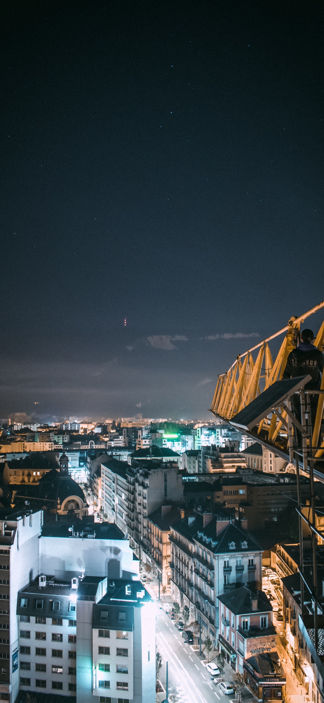 Yellow Metal Crane Near City Buildings During Night Time. Wallpaper in 1125x2436 Resolution