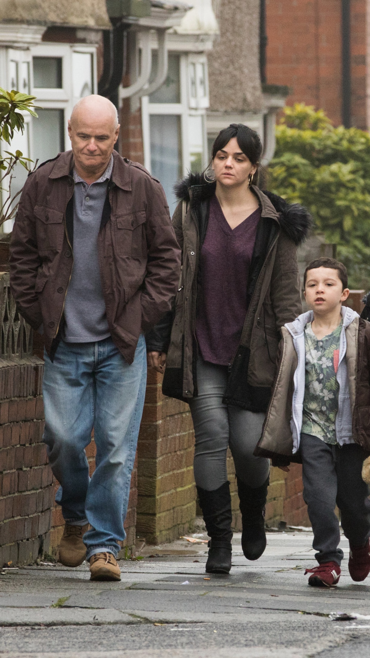 Hombre de Chaqueta Negra de Pie Junto a Una Mujer de Abrigo Marrón. Wallpaper in 750x1334 Resolution