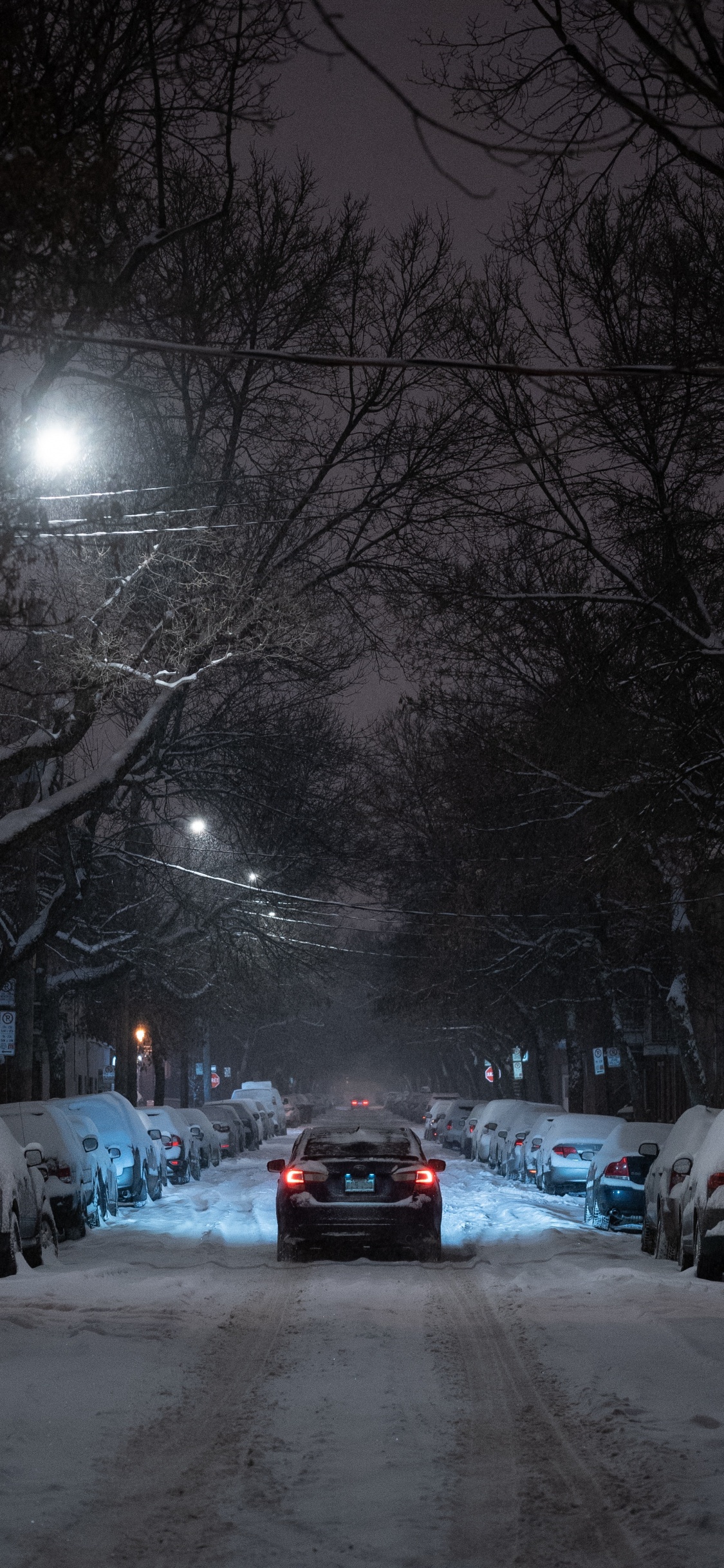 Autos Parken Nachts Auf Schneebedeckter Straße. Wallpaper in 1125x2436 Resolution