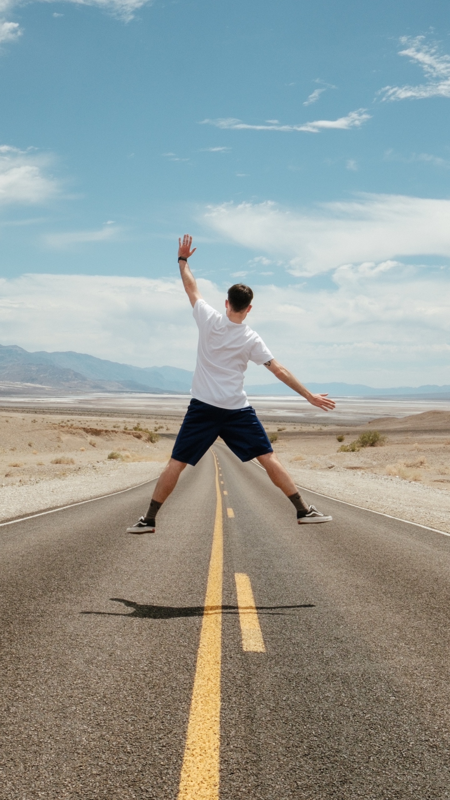 Mann in Weißem T-Shirt Und Schwarzen Shorts Läuft Auf Grauer Asphaltstraße Unter Blau Und. Wallpaper in 1440x2560 Resolution