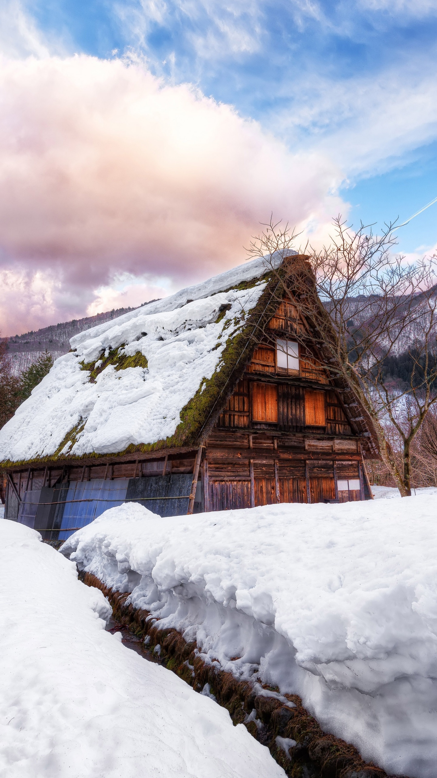 Casa de Madera Marrón Sobre Suelo Cubierto de Nieve Bajo Las Nubes Blancas y el Cielo Azul Durante el Día. Wallpaper in 1440x2560 Resolution