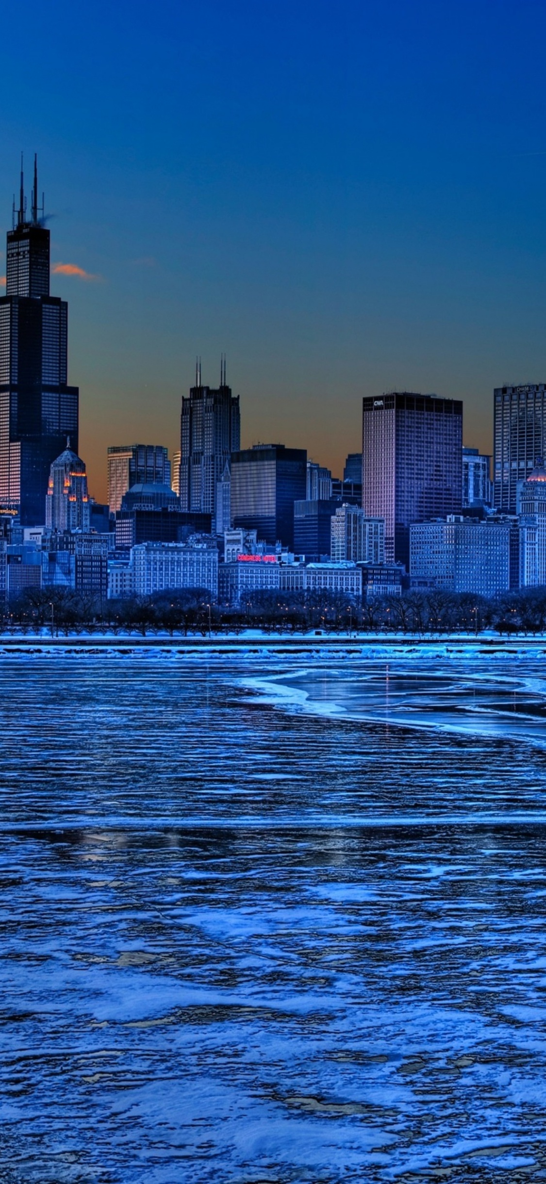 Skyline Der Stadt Über Gewässer Während Der Nacht. Wallpaper in 1125x2436 Resolution