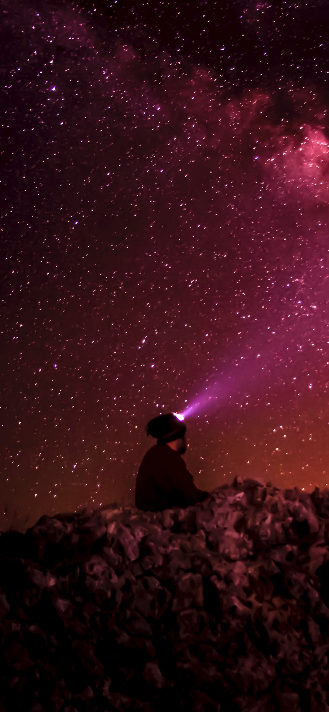 Man Sitting on Rock Under Starry Night. Wallpaper in 1125x2436 Resolution