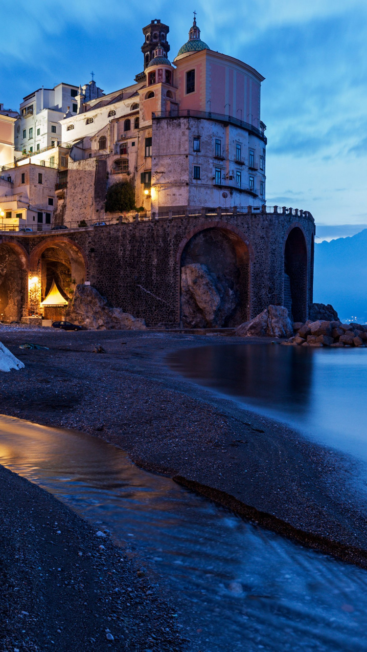 Edificio de Hormigón Marrón Cerca Del Cuerpo de Agua Durante la Noche. Wallpaper in 750x1334 Resolution