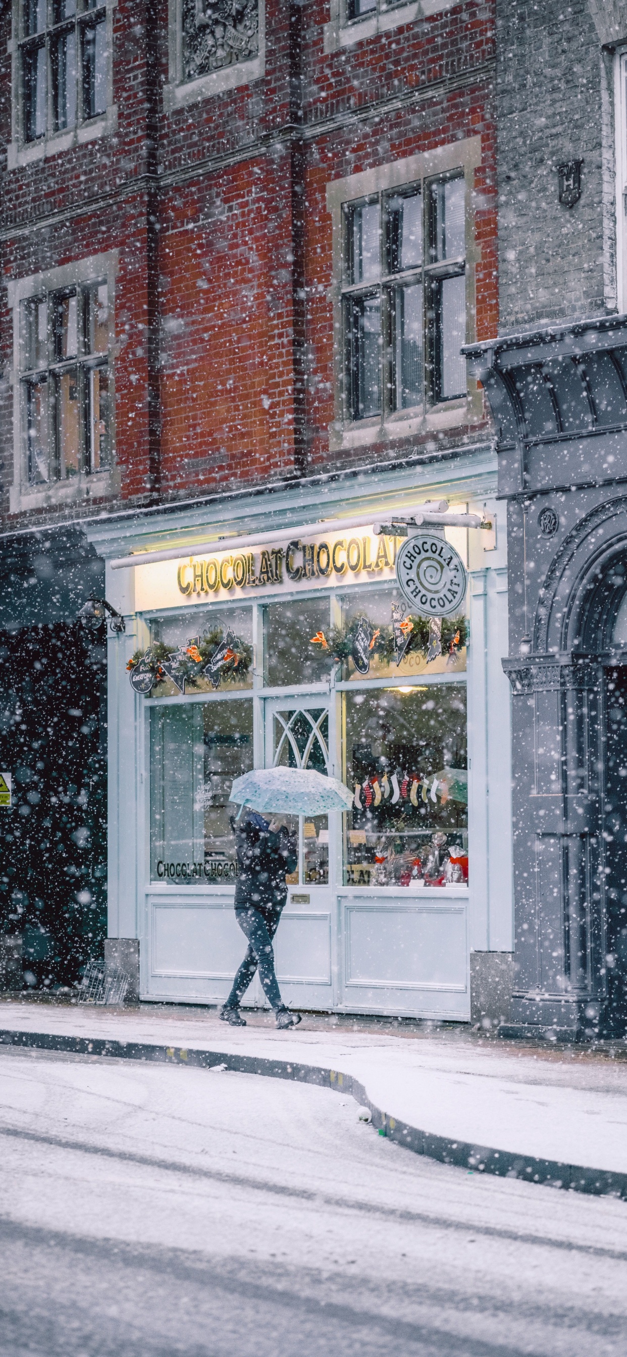 Person in Black Jacket and Black Pants Walking on Sidewalk During Daytime. Wallpaper in 1242x2688 Resolution