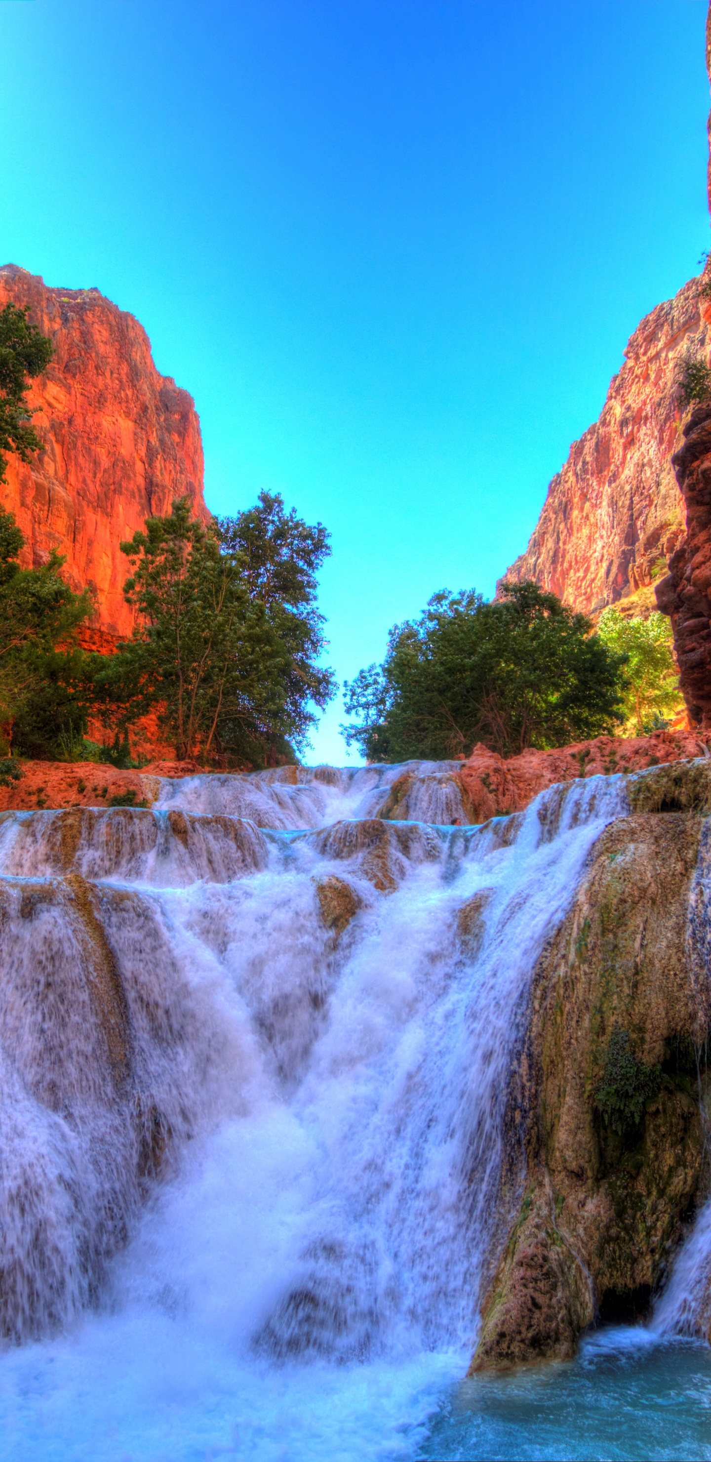 Cascadas Entre la Montaña Rocosa Marrón Bajo un Cielo Azul Durante el Día. Wallpaper in 1440x2960 Resolution