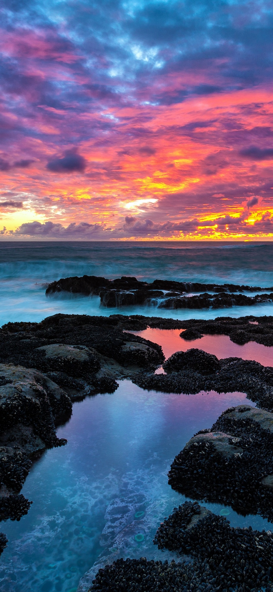 Rocas Marrones en la Orilla Del Mar Durante la Puesta de Sol. Wallpaper in 1125x2436 Resolution