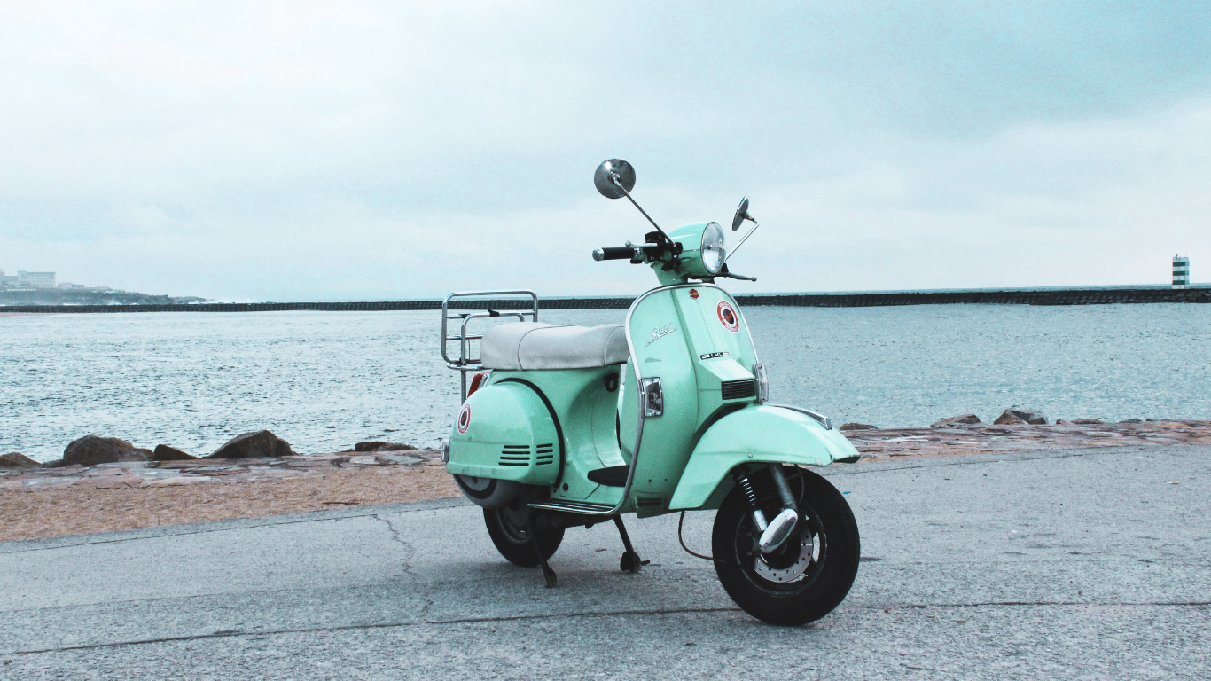 Green Motor Scooter Parked on Gray Concrete Pavement Near Body of Water During Daytime. Wallpaper in 1366x768 Resolution