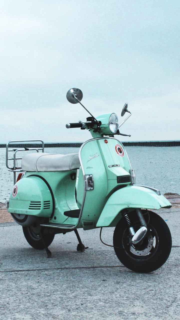 Green Motor Scooter Parked on Gray Concrete Pavement Near Body of Water During Daytime. Wallpaper in 720x1280 Resolution