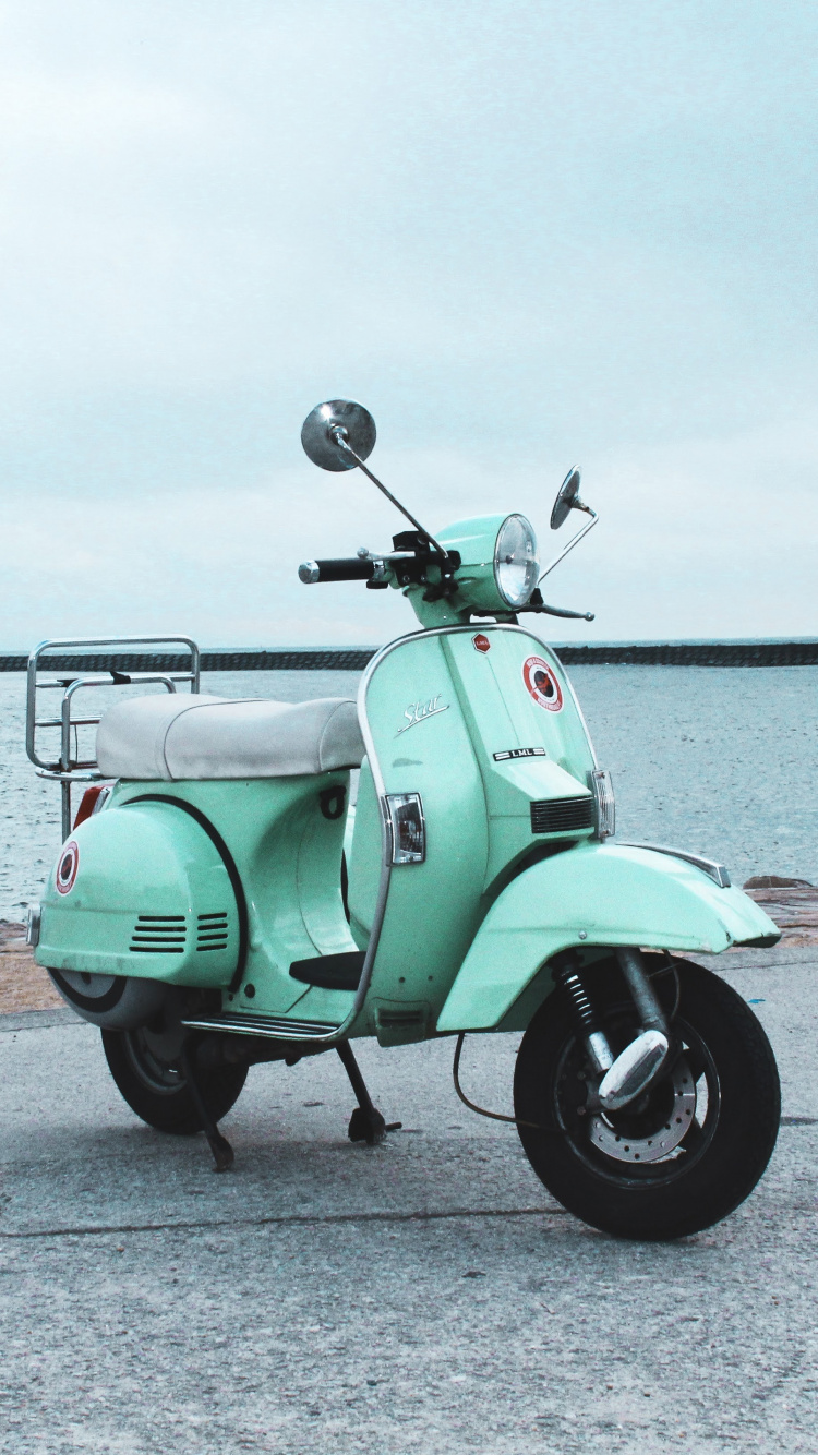 Green Motor Scooter Parked on Gray Concrete Pavement Near Body of Water During Daytime. Wallpaper in 750x1334 Resolution