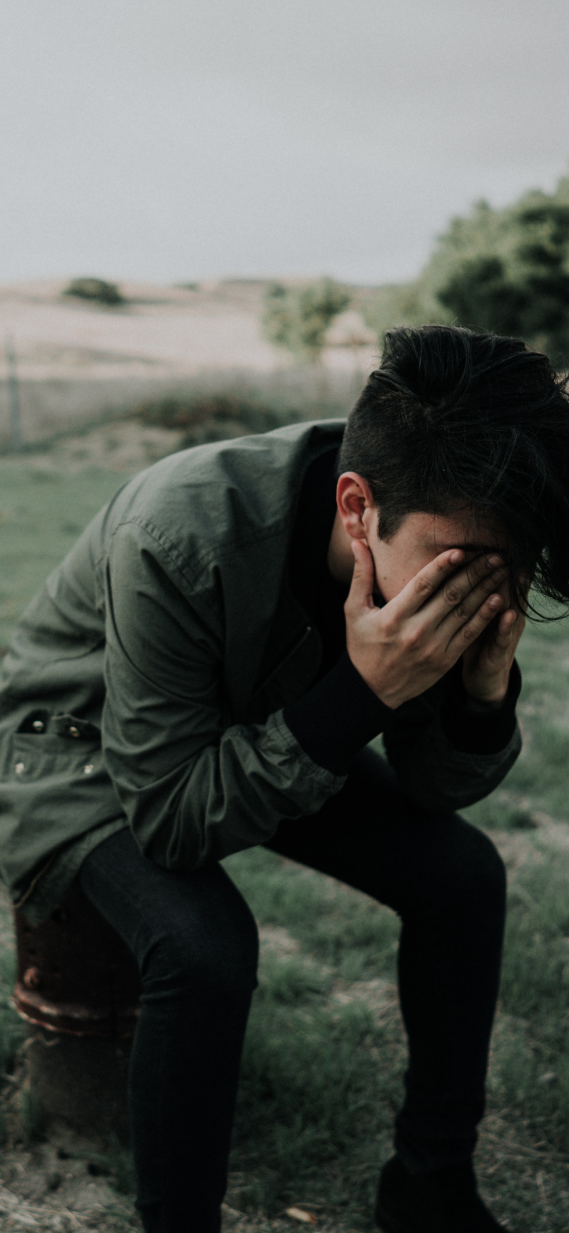 Man in Gray Jacket and Black Pants Sitting on Gray Sand During Daytime. Wallpaper in 1125x2436 Resolution
