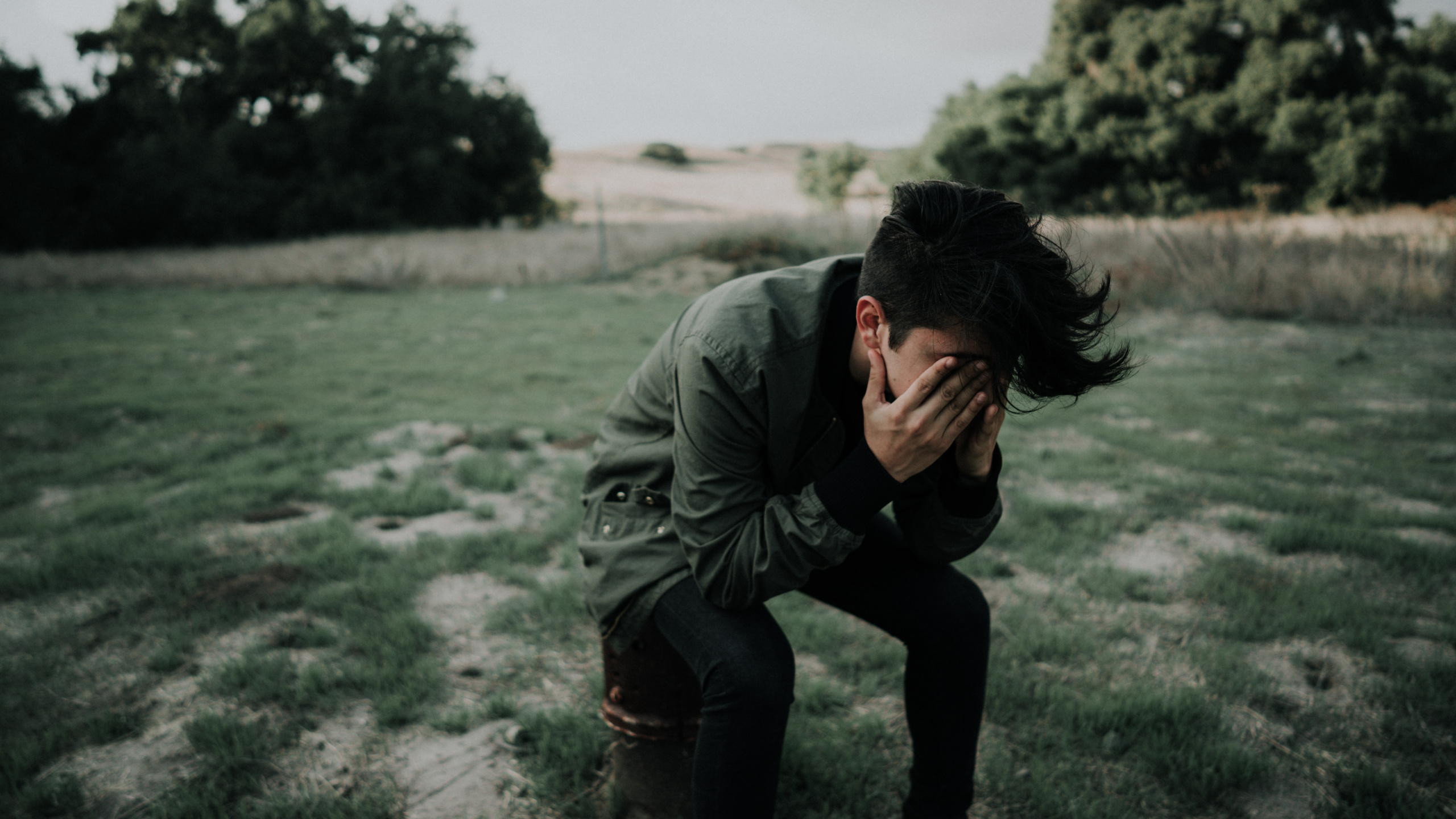 Man in Gray Jacket and Black Pants Sitting on Gray Sand During Daytime. Wallpaper in 2560x1440 Resolution