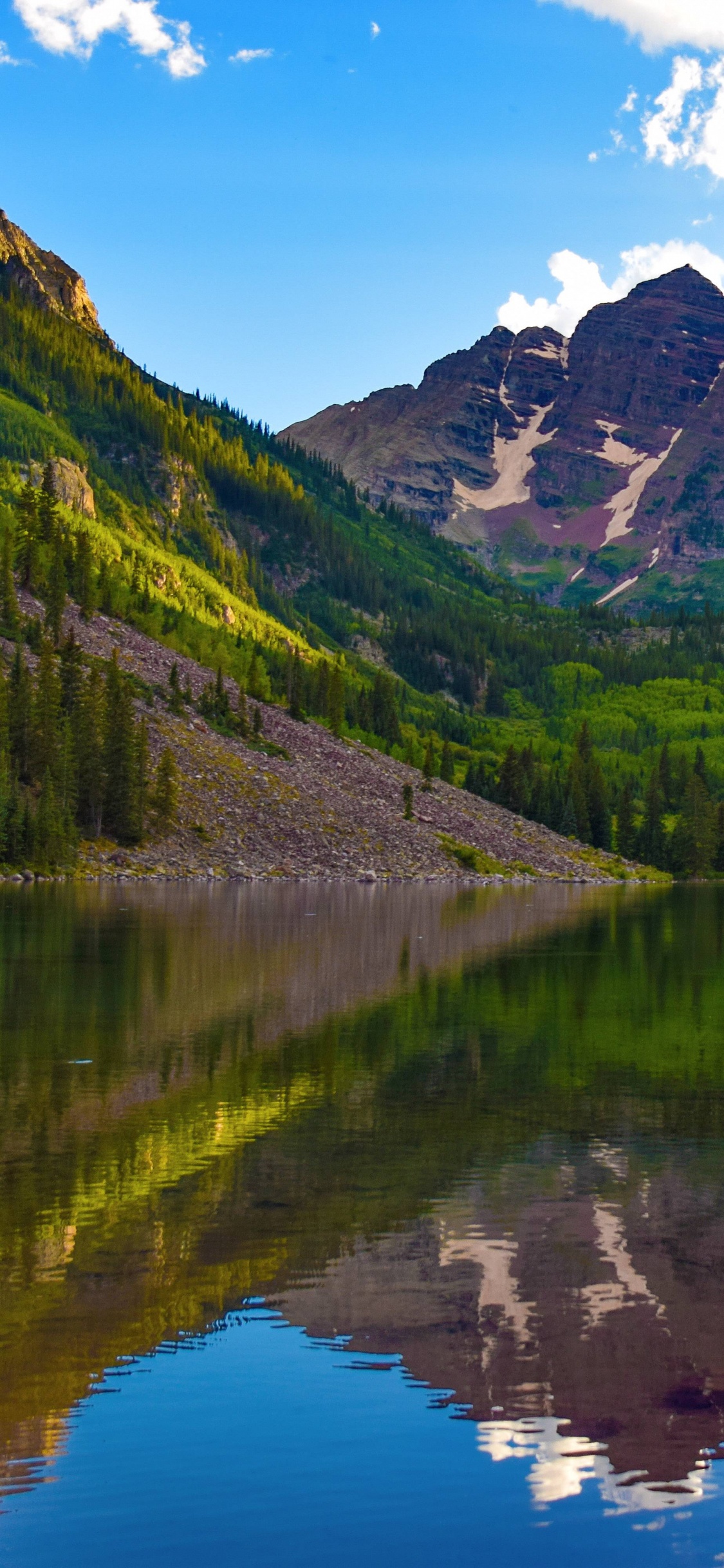 Green Mountains Beside Lake Under Blue Sky During Daytime. Wallpaper in 1125x2436 Resolution
