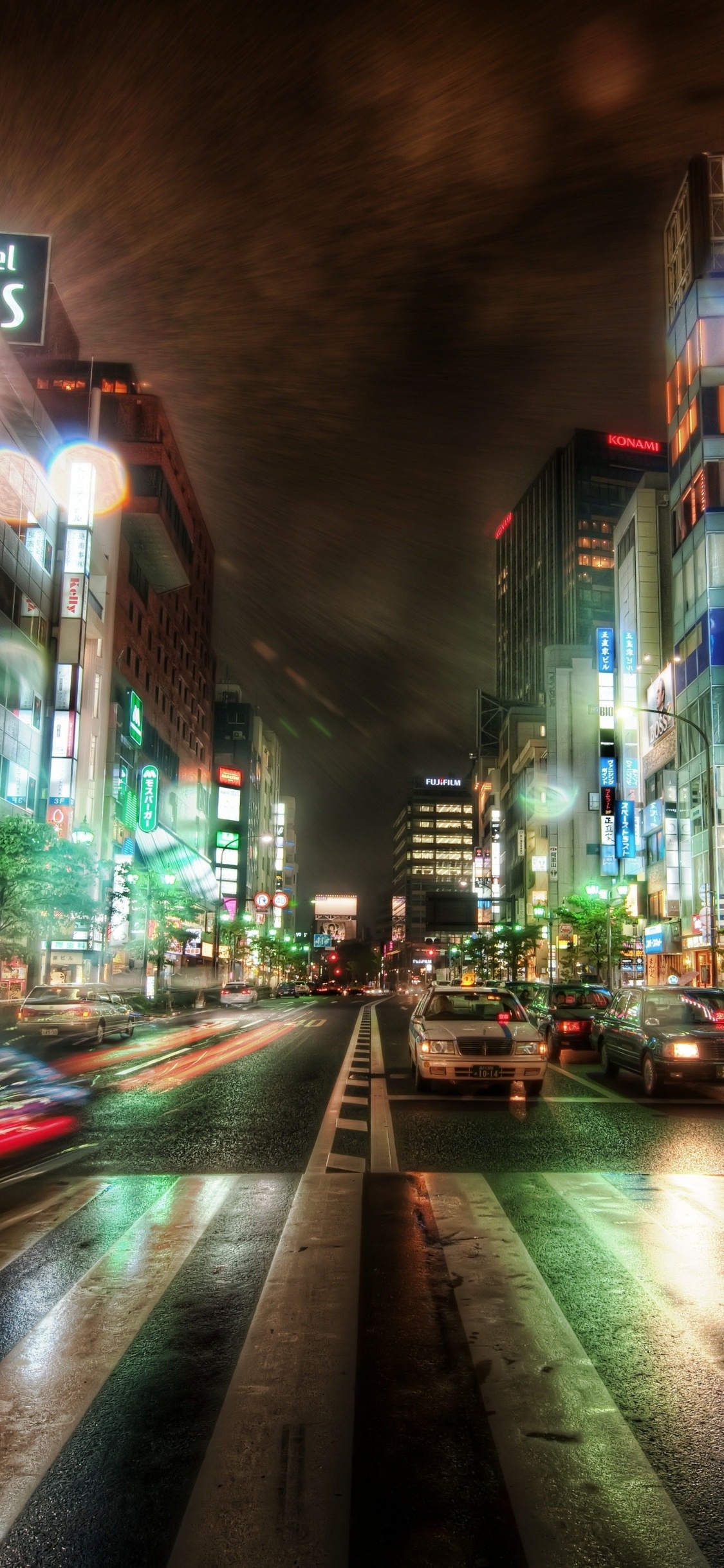 Autos Auf Der Straße Zwischen Hochhäusern Während Der Nacht. Wallpaper in 1125x2436 Resolution