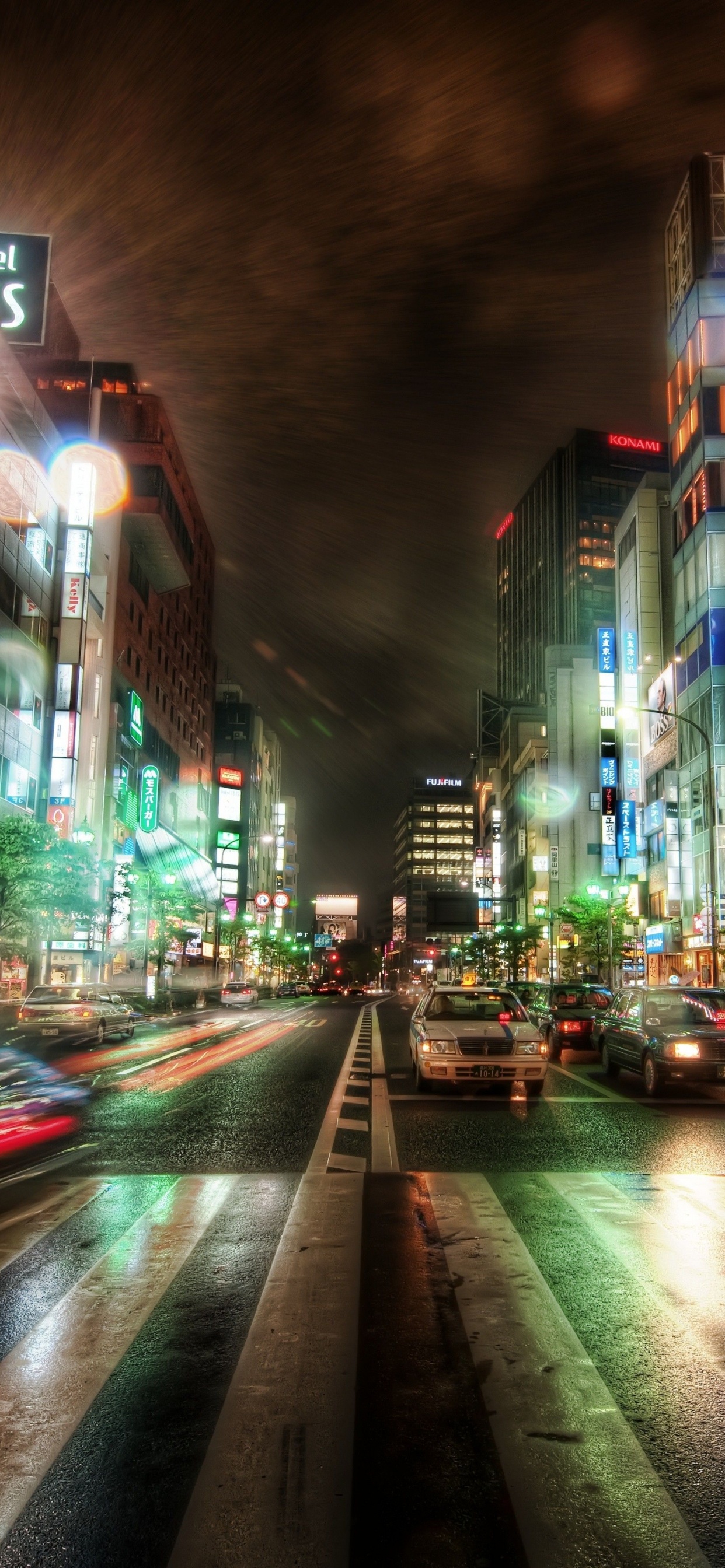 Autos Auf Der Straße Zwischen Hochhäusern Während Der Nacht. Wallpaper in 1242x2688 Resolution