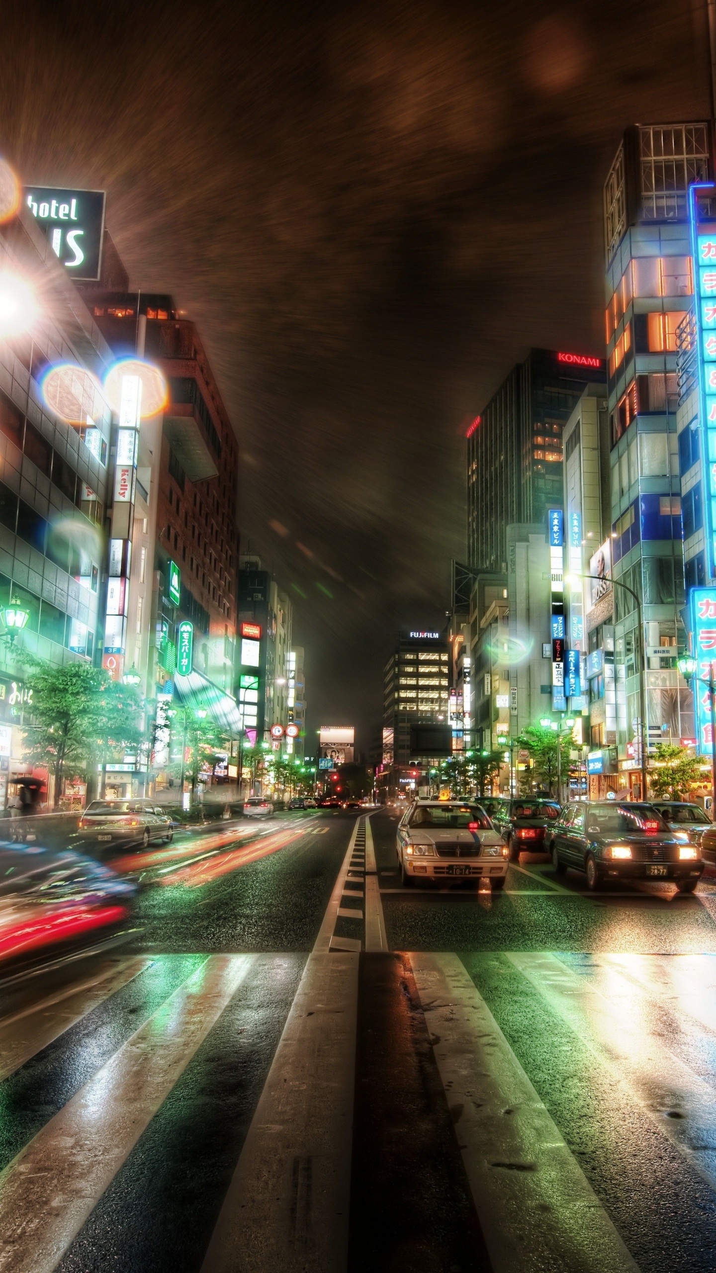 Autos Auf Der Straße Zwischen Hochhäusern Während Der Nacht. Wallpaper in 1440x2560 Resolution