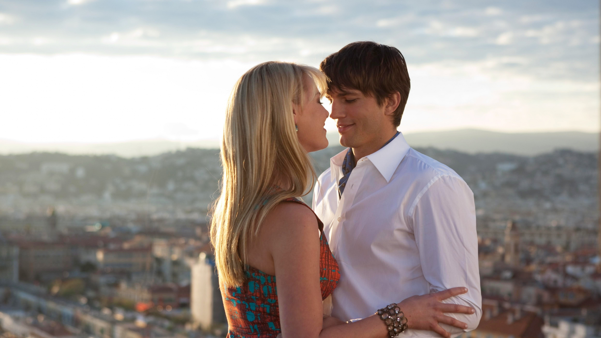 Man in White Suit Kissing Woman in Red and Blue Sleeveless Dress. Wallpaper in 2560x1440 Resolution