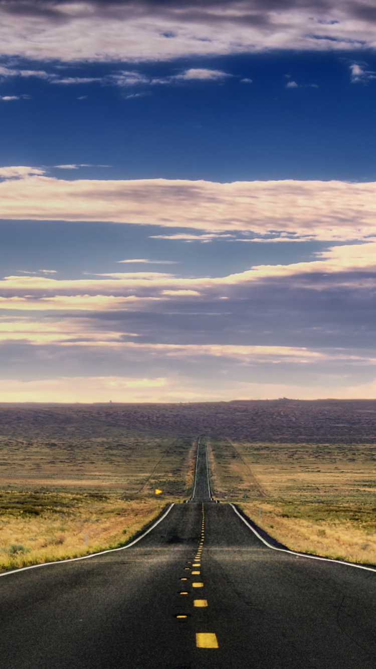 Black Asphalt Road Between Green Grass Field Under Blue and White Sunny Cloudy Sky During Daytime. Wallpaper in 750x1334 Resolution