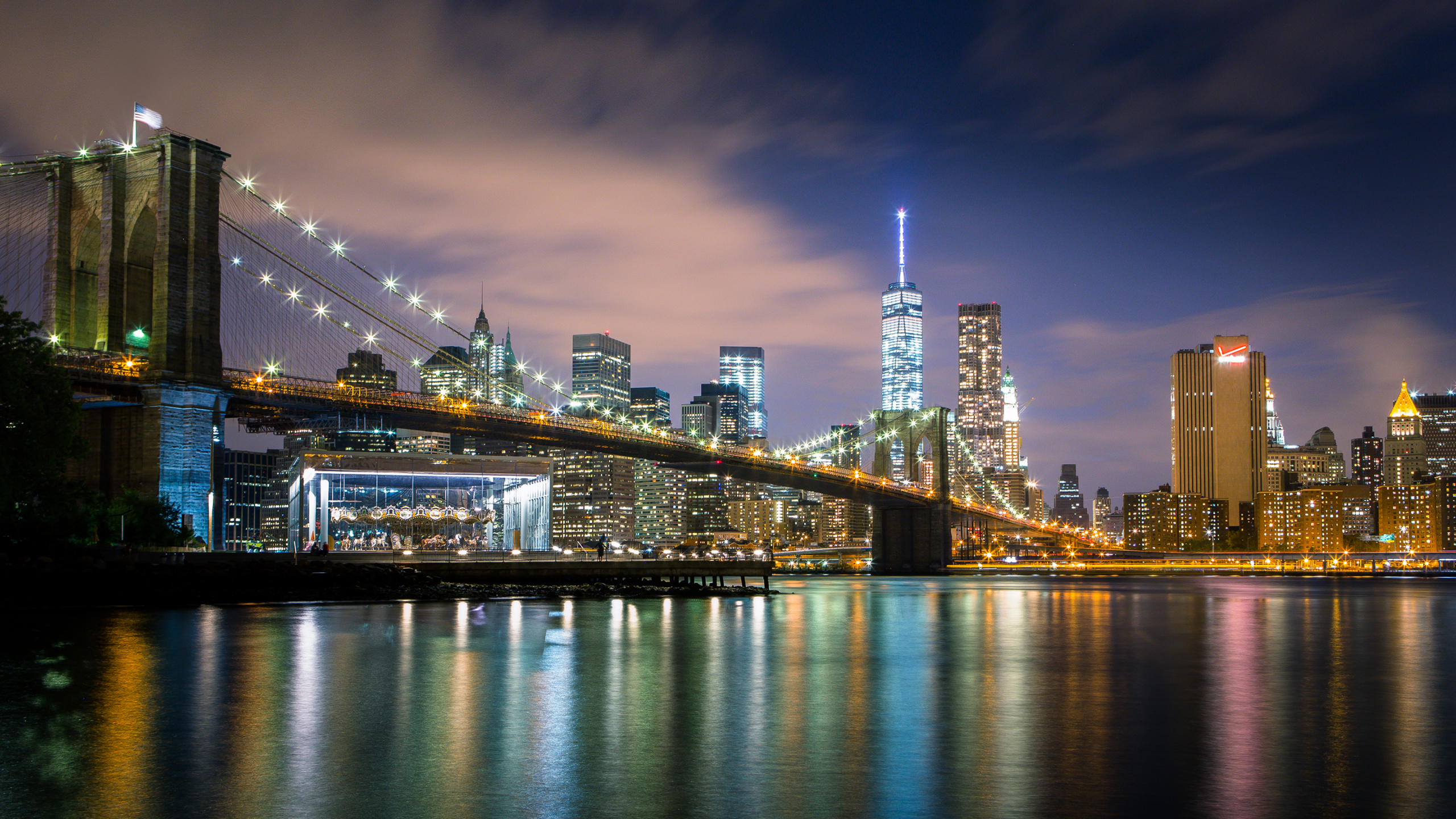 Lighted Bridge Over River Near City Skyline During Night Time. Wallpaper in 2560x1440 Resolution