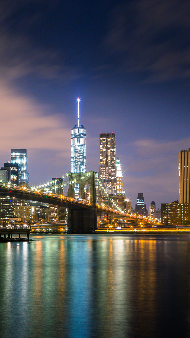Lighted Bridge Over River Near City Skyline During Night Time. Wallpaper in 750x1334 Resolution